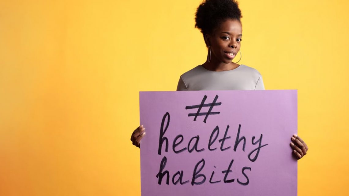 Portrait of a woman holding a healthy habits sign, set against a vibrant yellow background.