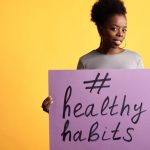 Portrait of a woman holding a healthy habits sign, set against a vibrant yellow background.