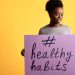 Portrait of a woman holding a healthy habits sign, set against a vibrant yellow background.